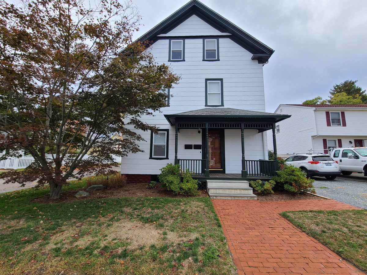 White three-story house with a dark green front porch and brick walkway